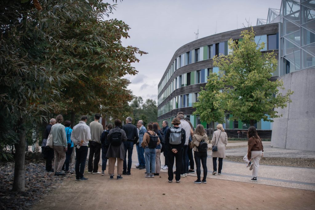 A group of people listening to a guide, while admiring the glass and wood facade with colorful elements of the Umweltbundesamt in Dessau